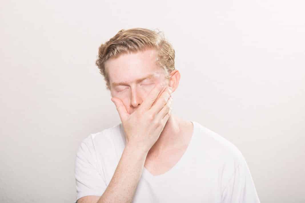 A young man puts his hand across his face with a pained expression