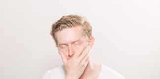 A young man puts his hand across his face with a pained expression
