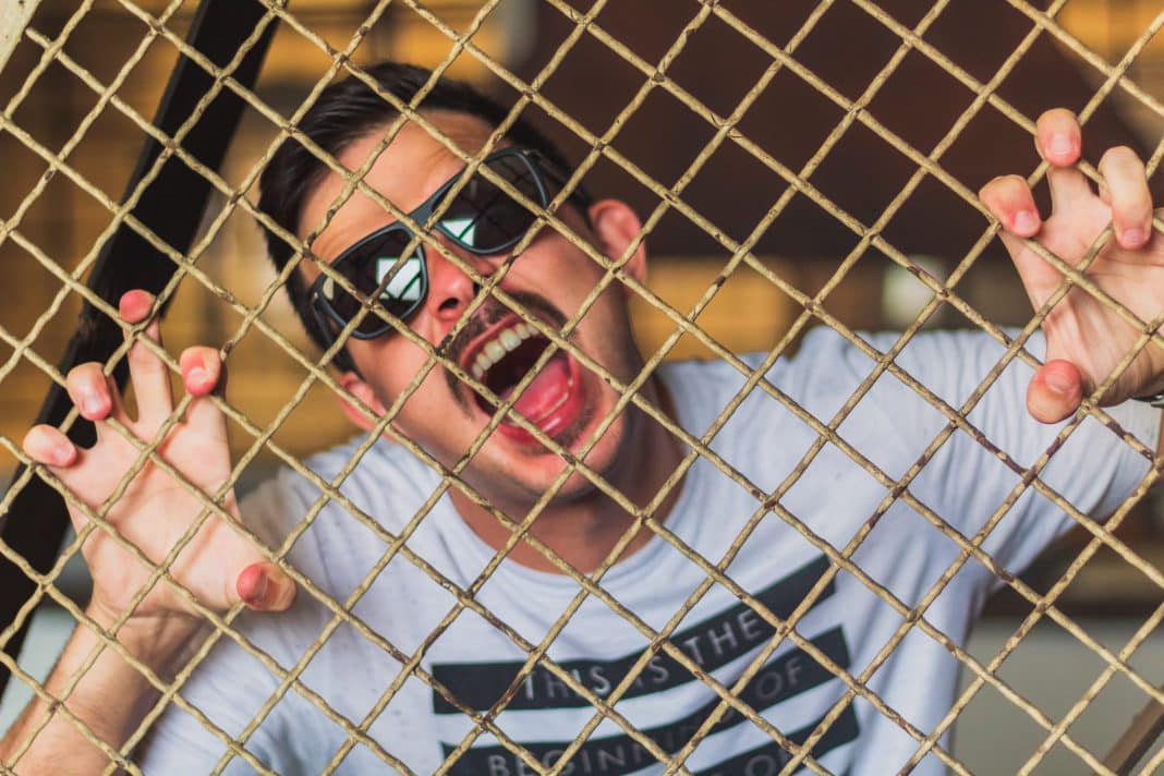 A man sticks his tongue on a metal fence.