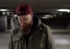 A bearded man walking through a car park with an unhappy expression.