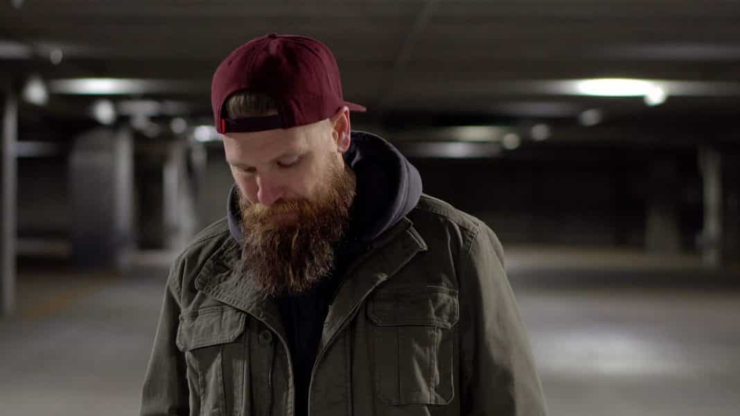 A bearded man walking through a car park with an unhappy expression.