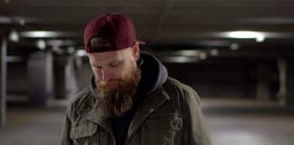 A bearded man walking through a car park with an unhappy expression.