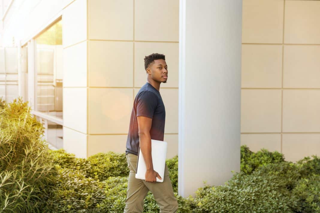 man holding laptop walking towards building