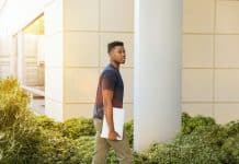 man holding laptop walking towards building