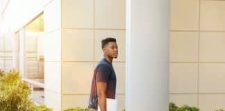 man holding laptop walking towards building