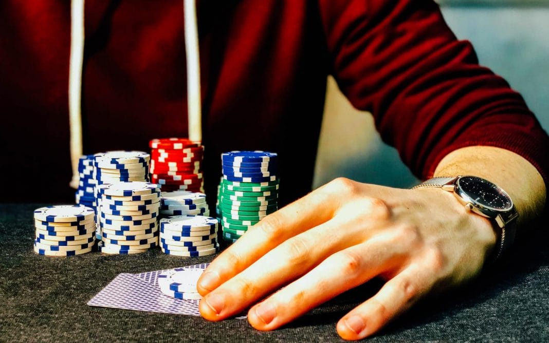 person holding playing cards beside poker chips