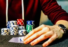 person holding playing cards beside poker chips