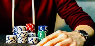 person holding playing cards beside poker chips