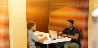 man sitting on black leather bench holding gray laptop computer on top of white wooden table