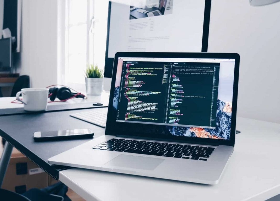 A MacBook with lines of code on its screen on a busy desk