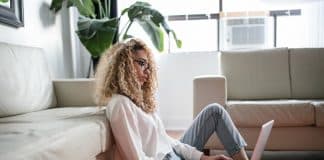 woman sitting on floor and leaning on couch using laptop