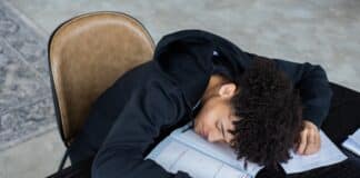 High angle of exhausted African American student resting on opened textbook and papers while preparing for exam