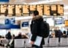 man standing inside airport looking at LED flight schedule bulletin board