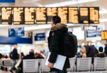 man standing inside airport looking at LED flight schedule bulletin board