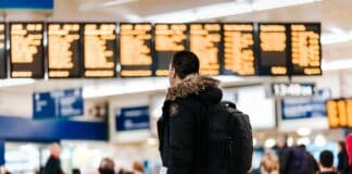 man standing inside airport looking at LED flight schedule bulletin board