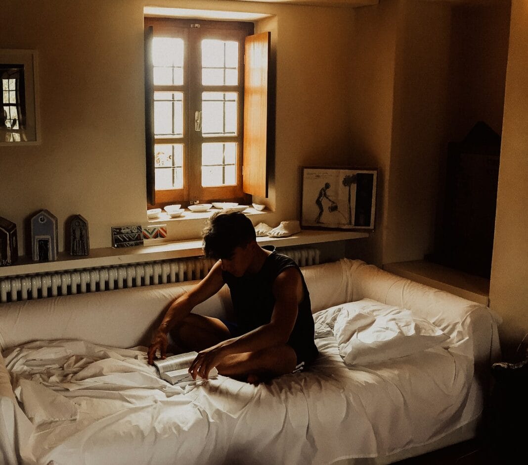 man sitting on bed beside opened window